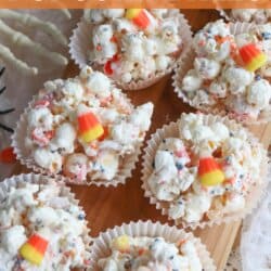 Popcorn balls with Halloween sprinkles and candy corn in cupcake liners on a wooden cutting board.