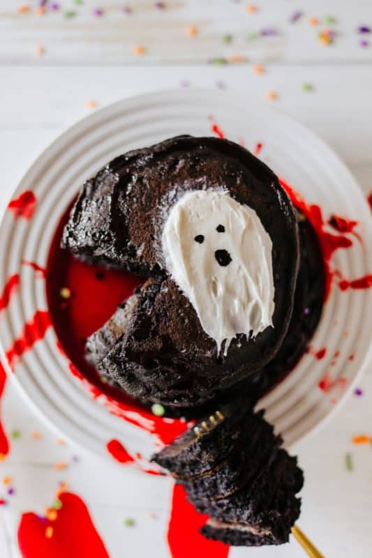 Stack of black pancakes with red syrup and white frosting in the shape of a ghost.