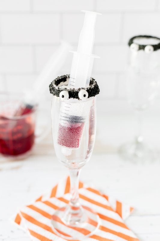 Champagne glass with a syringe in it with red grenadine.
