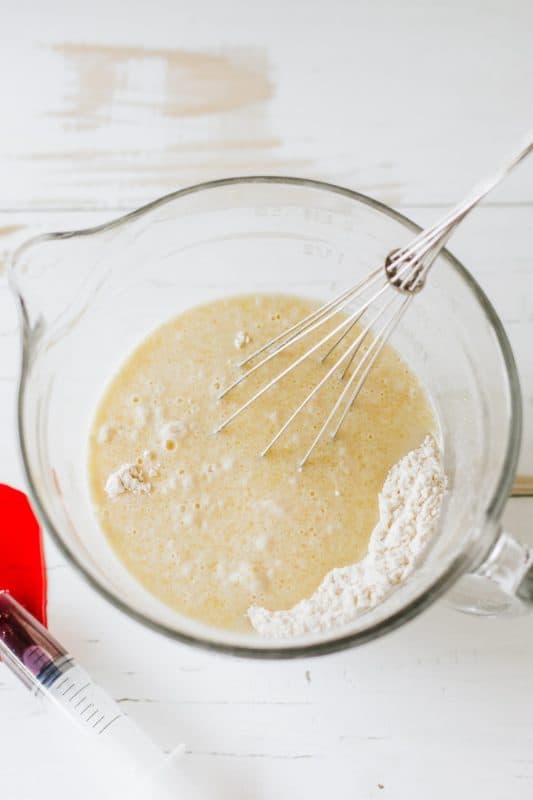 Ingredients for Halloween pancakes in a clear mixing bowl with a whisk.