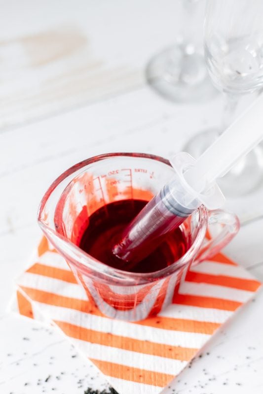 Red grenadine in a clear measuring cup with a syringe in it.