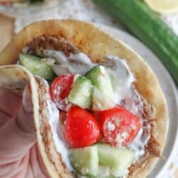 Tortilla with cooked ground turkey, diced cucumber, tomato and tzatziki sauce held in a hand.
