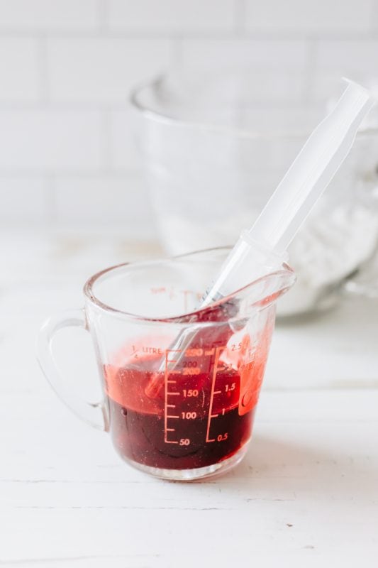 Red syrup in a small clear glass with a syringe.