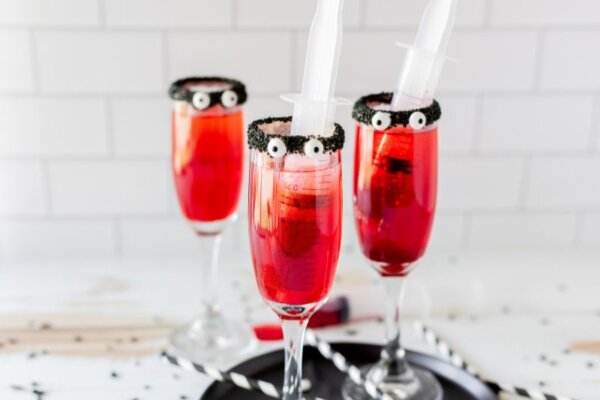 Red drinks in tall cocktail glasses with black rims and candy eyes.