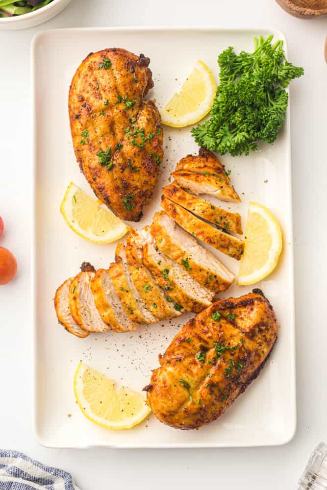 Air fried chicken breast garnished with fresh parsley and slices of lemon on a white serving plate.