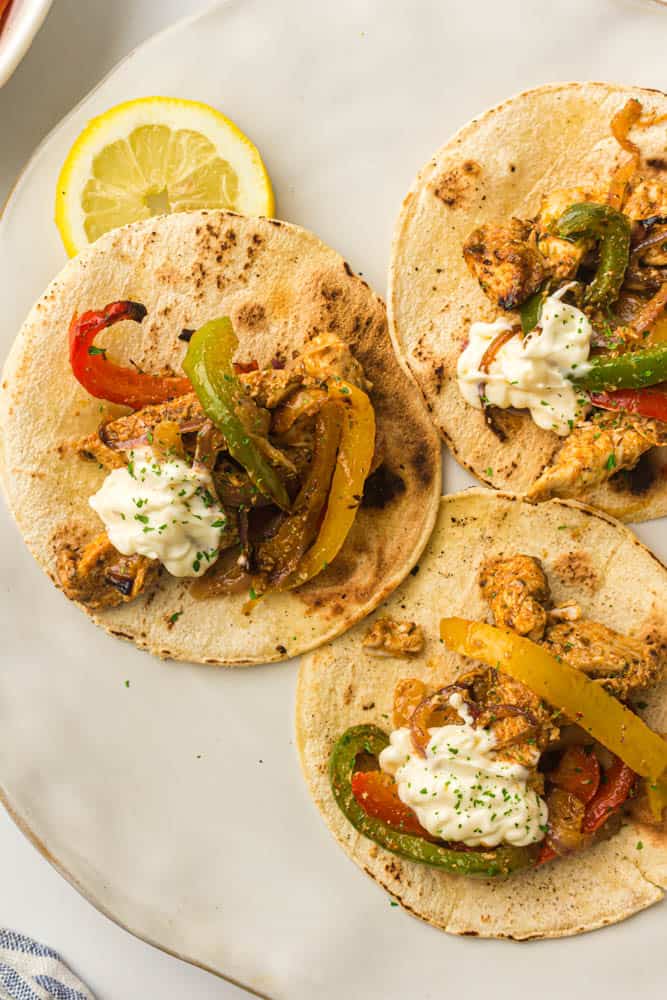 Chicken fajitas on a white plate with a lemon slice as garnish.