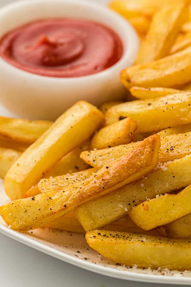 Seasoned french fries on a white plate and a small bowl of ketchup.