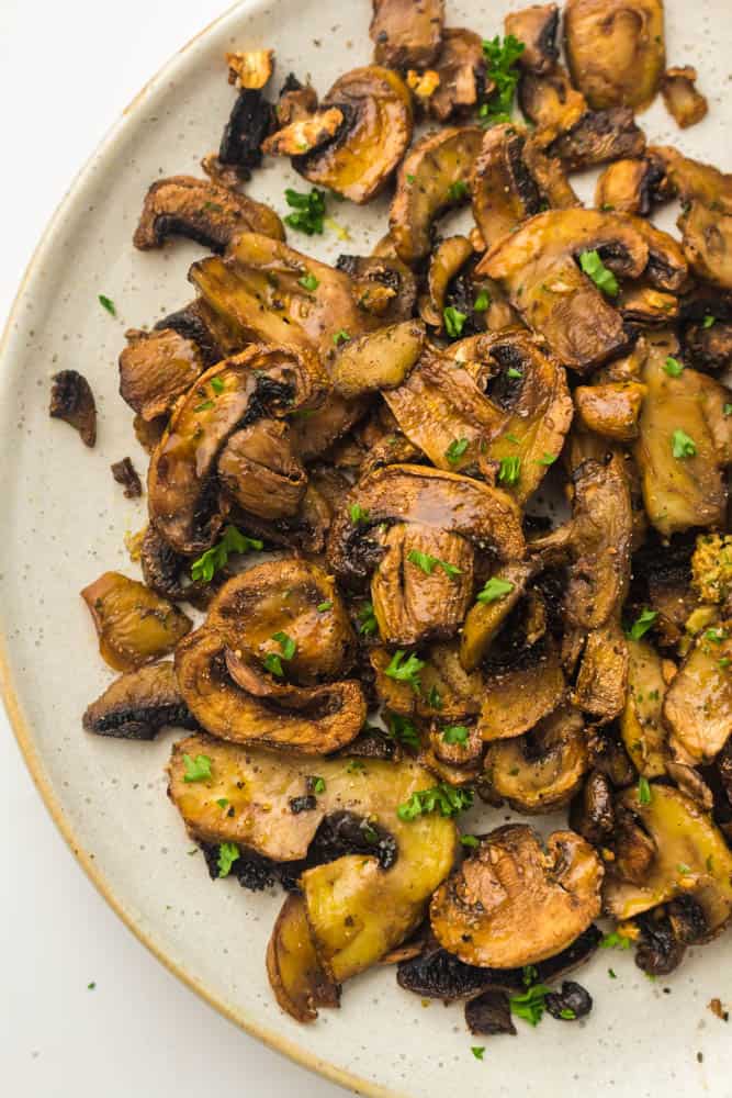 Fried mushrooms garnished with parsley on a white plate.