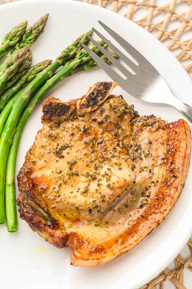 Air fryer pork chop and a side of asparagus and a fork on a white plate and textured place mat.