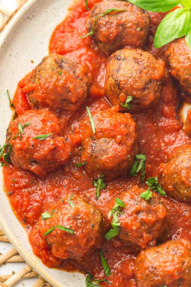 Plate of meatballs covered in spaghetti sauce with basil garnish.