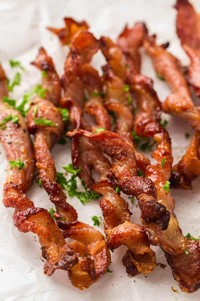 Crispy, twisted bacon strips laid out on a parchment-lined baking tray with a parsley garnish.