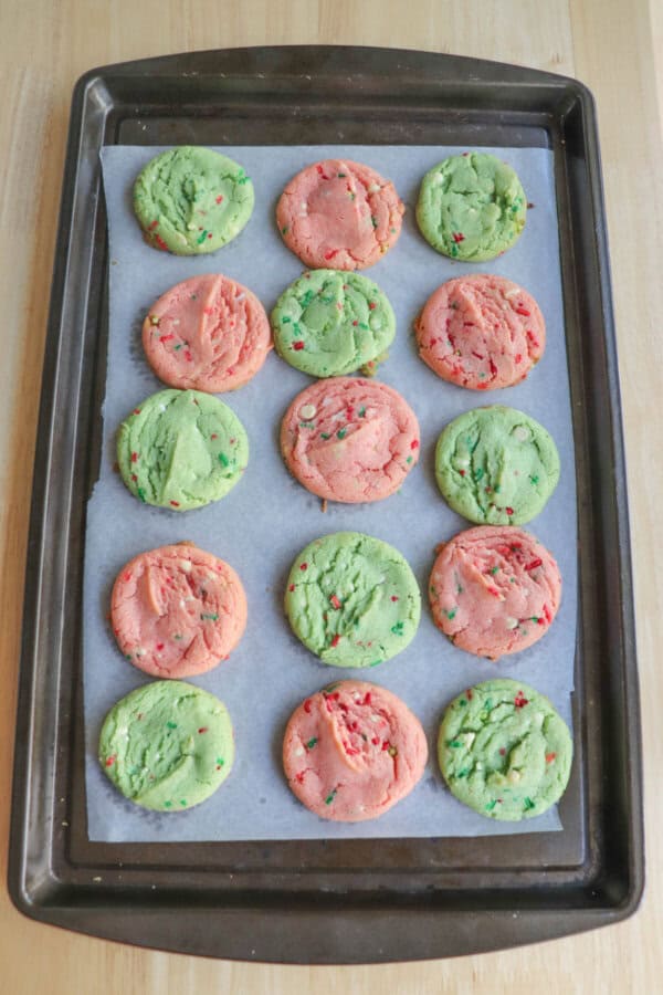 Baked pink and green cookies on a parchment paper lined baking sheet.