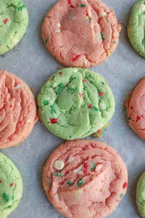 Pink and green cookies with Christmas sprinkles on a parchment paper lined baking sheet.