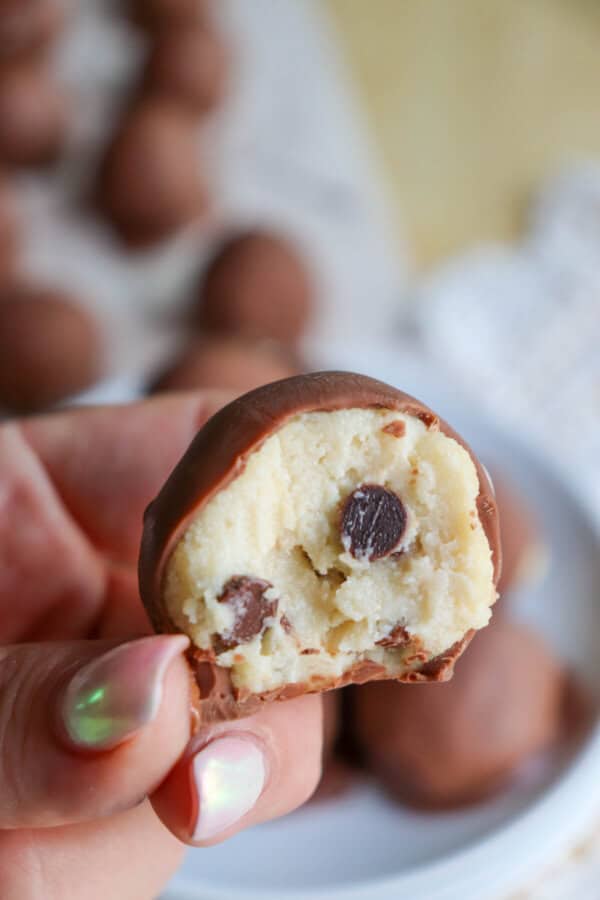 Cookie dough ball covered in chocolate with a bite taken out held in a hand.