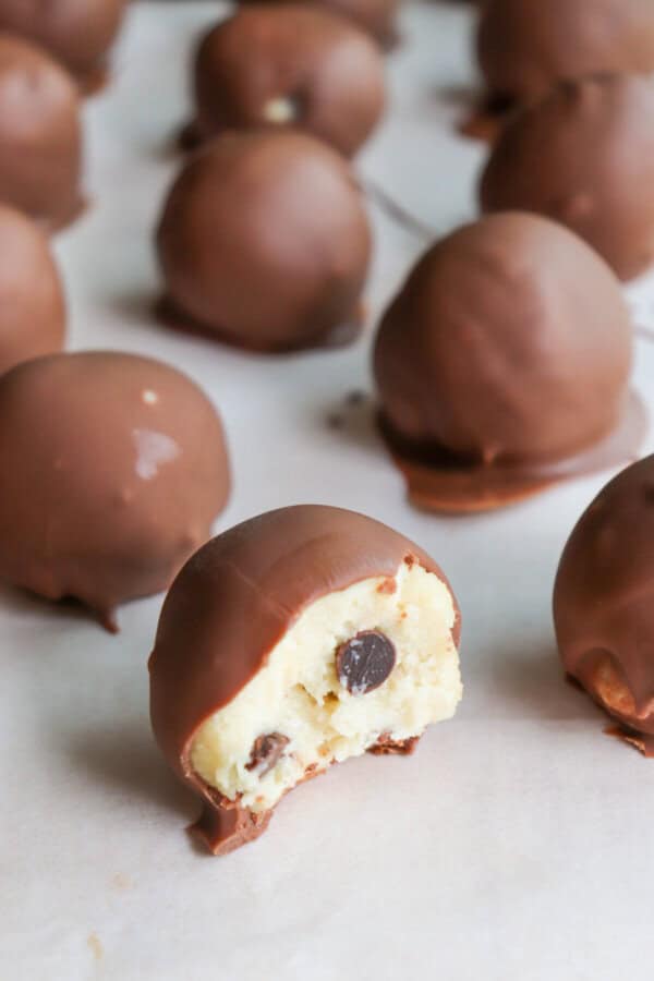Cookie dough ball covered in chocolate with a bite taken out on a piece of parchment paper.