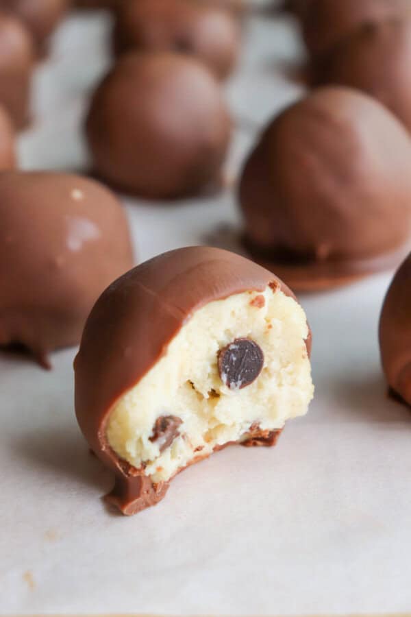 Cookie dough ball covered in chocolate with a bite taken out on a piece of parchment paper.