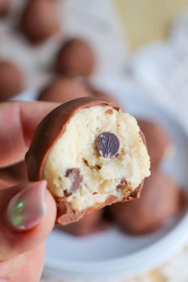 Cookie dough ball covered in chocolate with a bite taken out held in a hand.