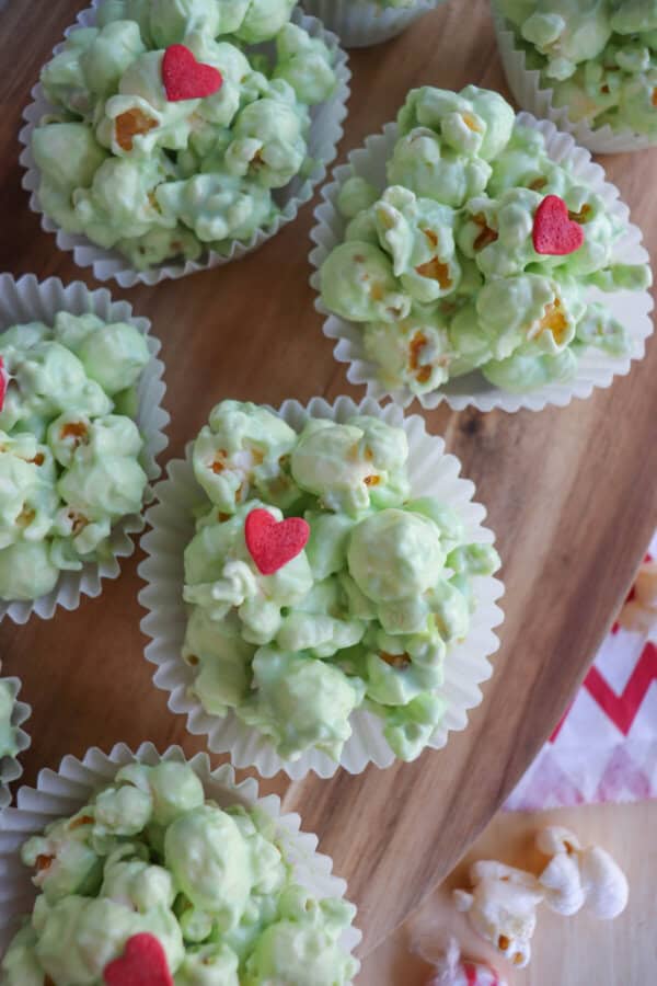 Green popcorn balls in white cupcake liners topped with a red candy heart.
