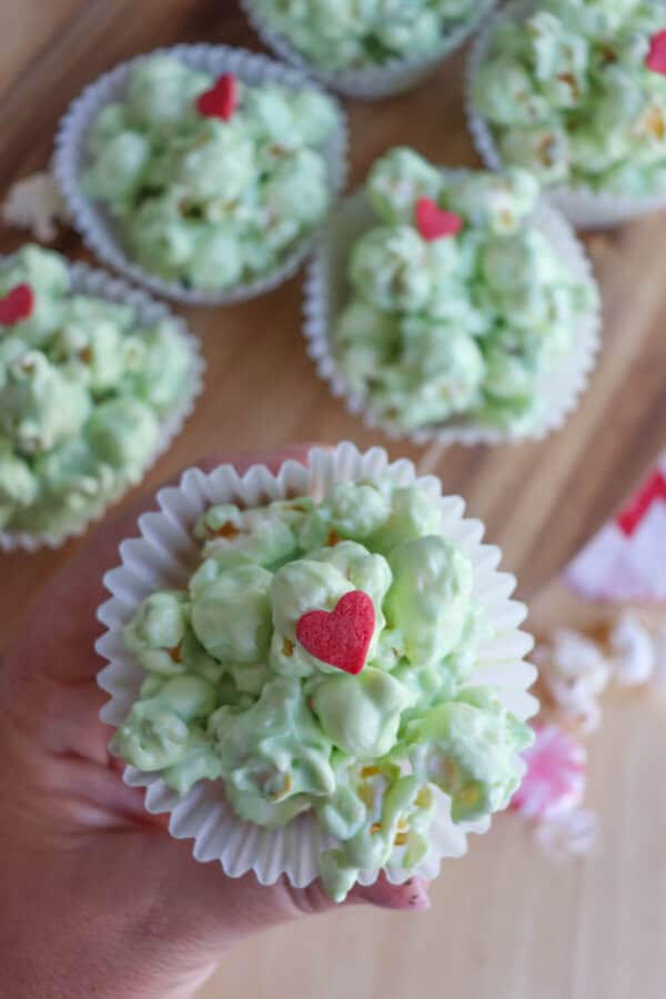 Green popcorn balls in white cupcake liners topped with a red candy heart.