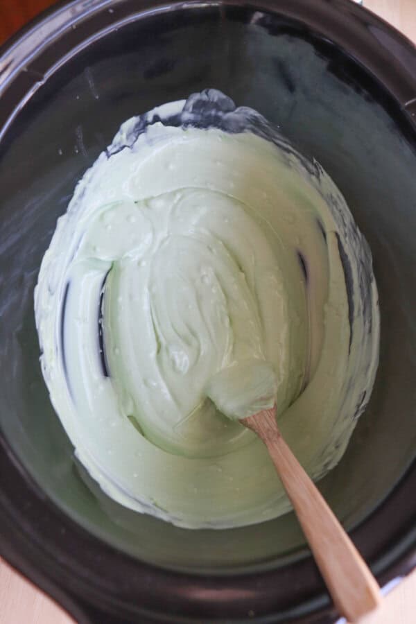 Green melted chocolate stirred in a large black crockpot.