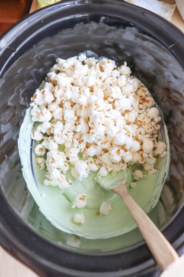 Popcorn and melted green chocolate in a black crock pot.