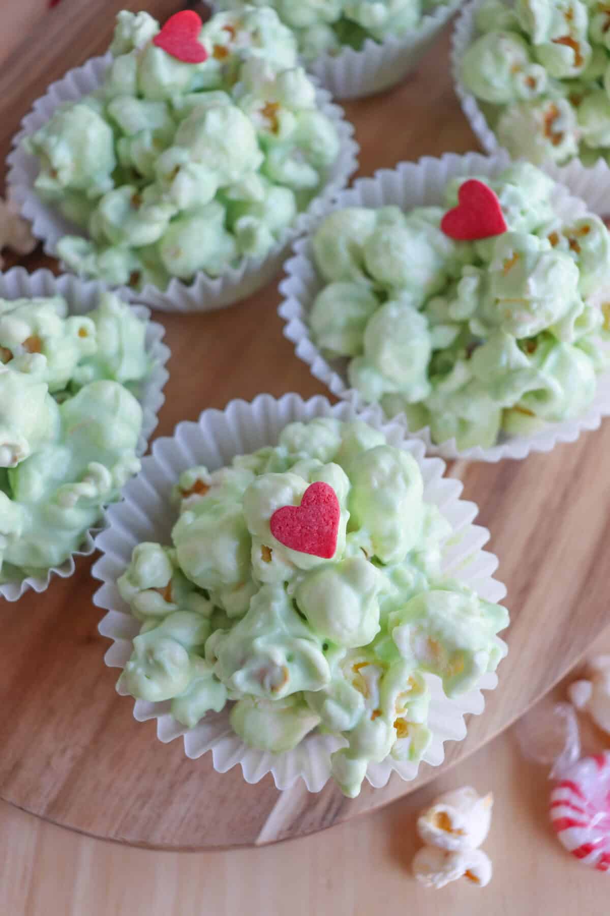 Green popcorn balls in white cupcake liners topped with a red candy heart.