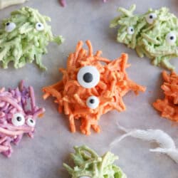 Colorful chocolate covered haystacks with candy eyes on a sheet of parchment paper.