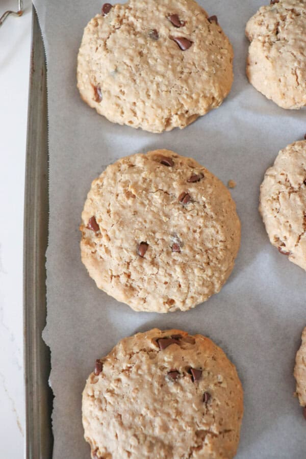Large oatmeal chocolate chip cookies on a parchment paper lined baking sheet.