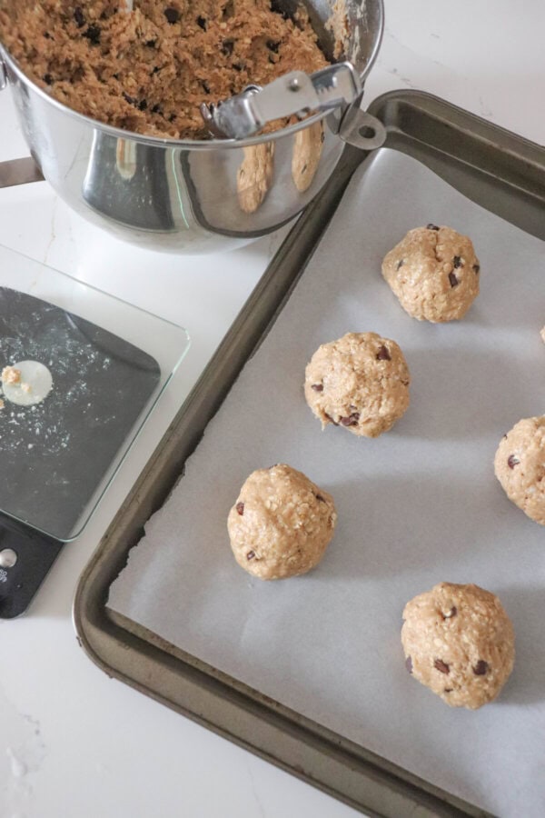 Balls of cookie dough on a parchment paper lined cookie sheet with a scale next to it.