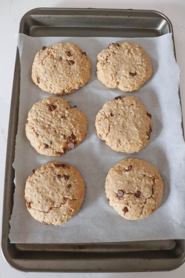 Six large oatmeal chocolate chip cookies on a parchment paper lined baking sheet.