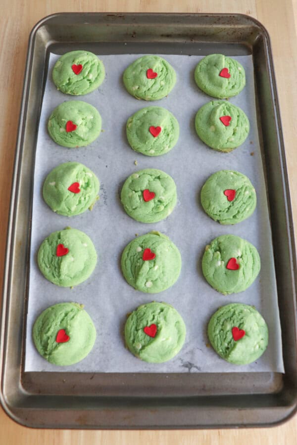 Green cookies with a red candy heart baked on a parchment paper lined cookie sheet.