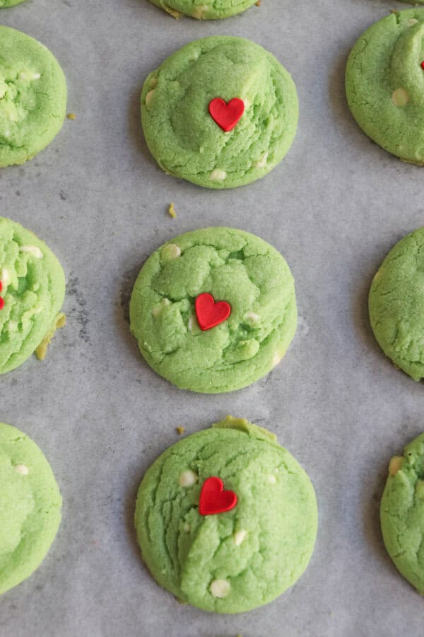 Green cookies with a red candy heart baked on a parchment paper lined cookie sheet.