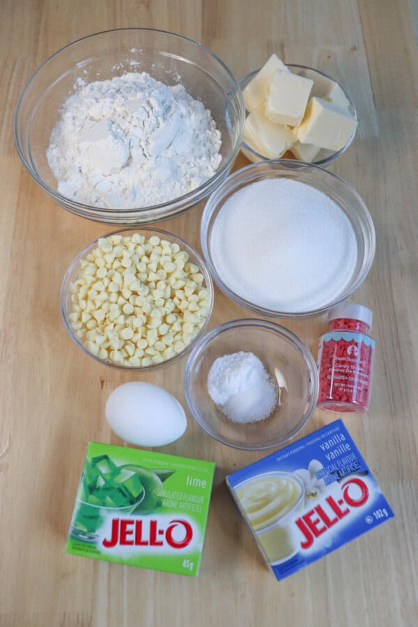 Ingredients for grinch pudding cookies in clear glass bowls on a wooden table.