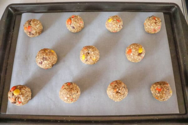Oatmeal cookie dough balls on a parchment paper lined baking sheet.