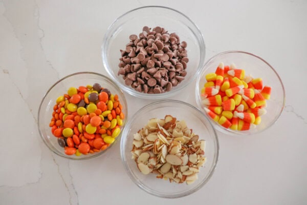 Ingredients for Halloween candy cookies in clear glass bowls on a white counter.