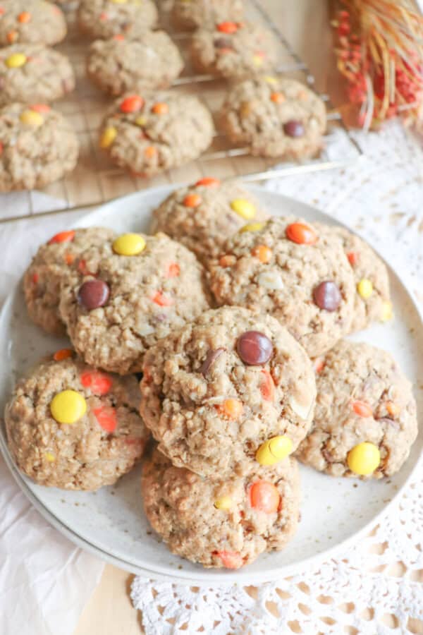 Oatmeal cookies with chocolate chips, orange and yellow M&Ms stacked on a cream plate.