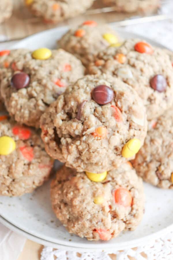 Oatmeal cookies with chocolate chips, orange and yellow M&Ms stacked on a cream plate.
