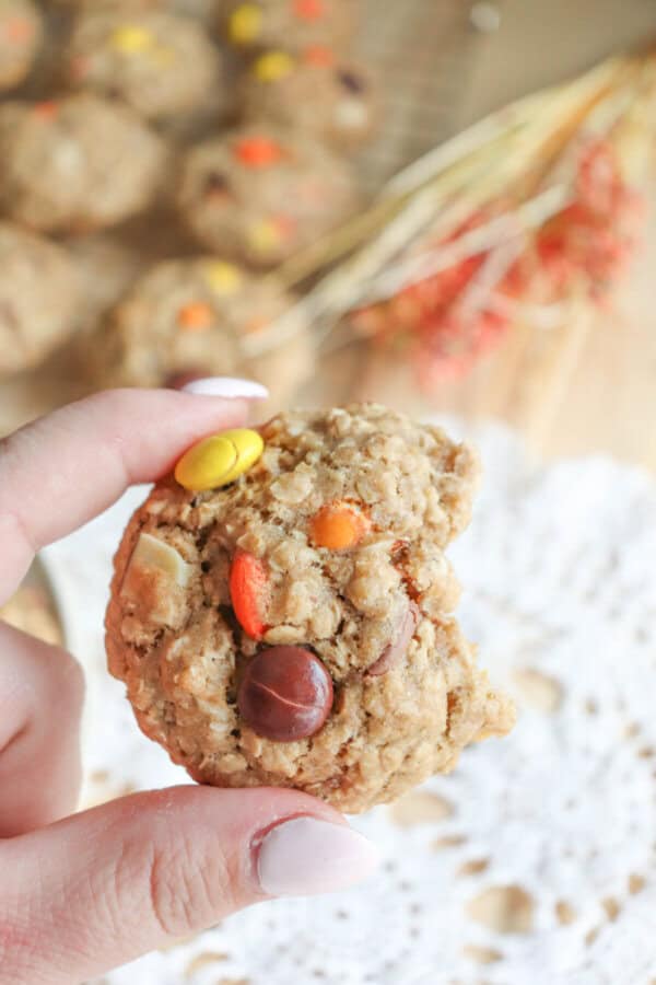 Oatmeal cookies with chocolate chips, orange and yellow M&Ms stacked on a cream plate.