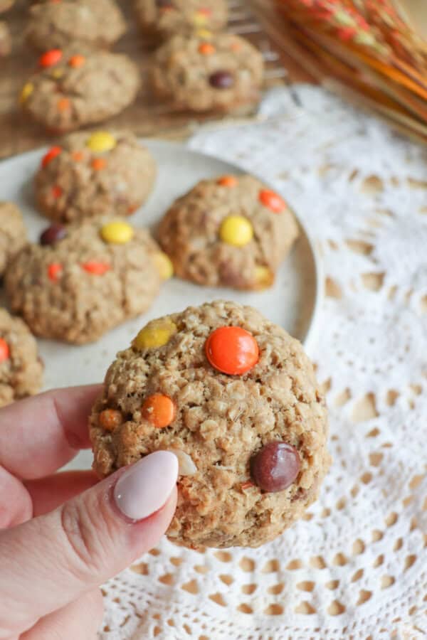 Oatmeal cookies with chocolate chips, orange and yellow M&Ms stacked on a cream plate.