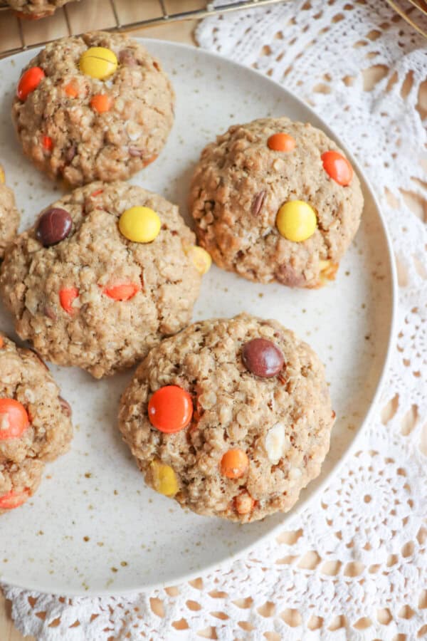 Oatmeal cookies with chocolate chips, orange and yellow M&Ms stacked on a cream plate.