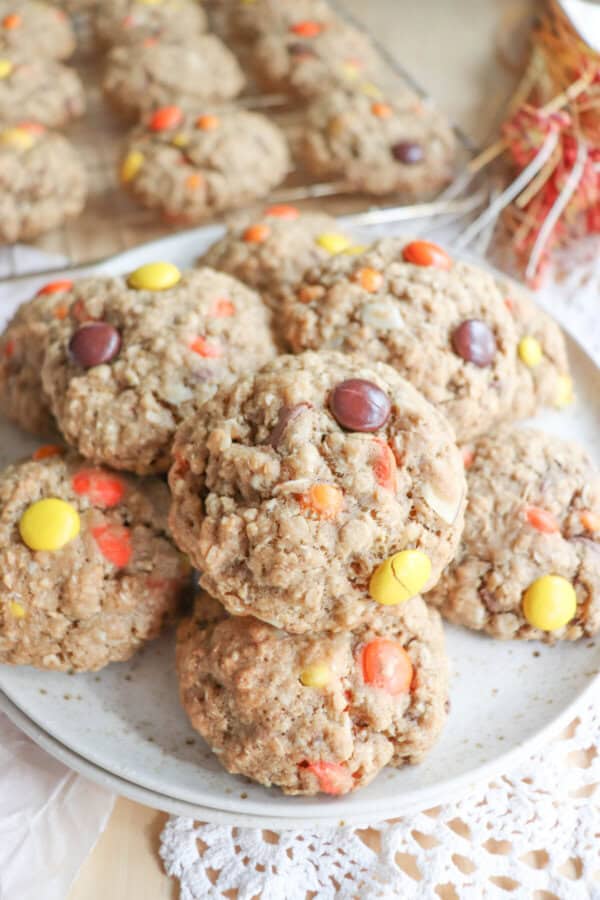 Oatmeal cookies with chocolate chips, orange and yellow M&Ms stacked on a cream plate.