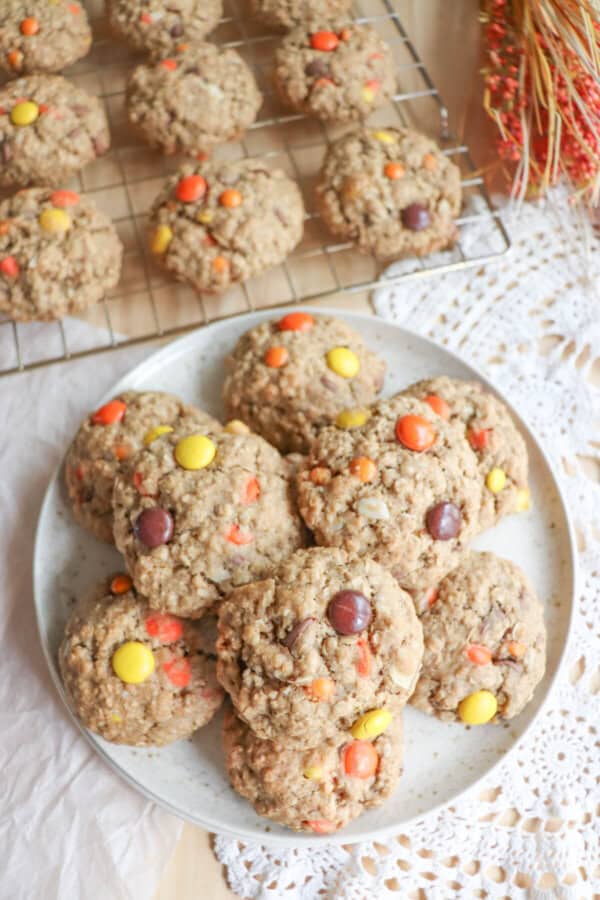 Oatmeal cookies with chocolate chips, orange and yellow M&Ms stacked on a cream plate.