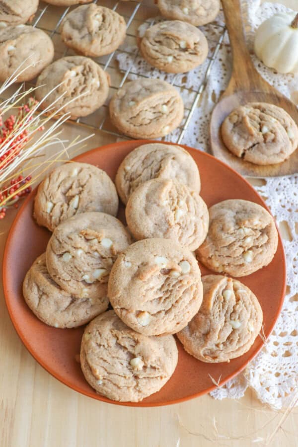 Caramel colored pumpkin spice cookies with white chocolate chips stacked on an orange plate.