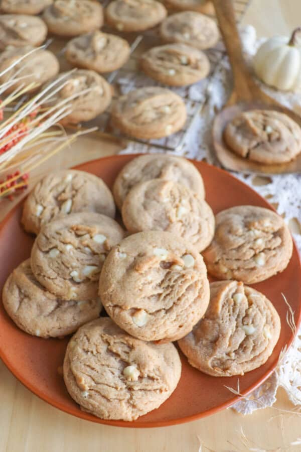 Caramel colored pumpkin spice cookies with white chocolate chips stacked on an orange plate.
