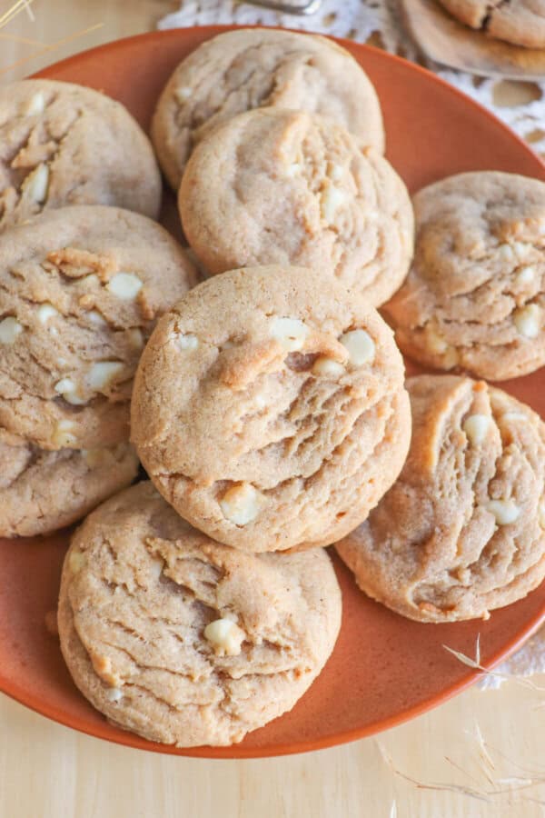 Caramel colored pumpkin spice cookies with white chocolate chips stacked on an orange plate.