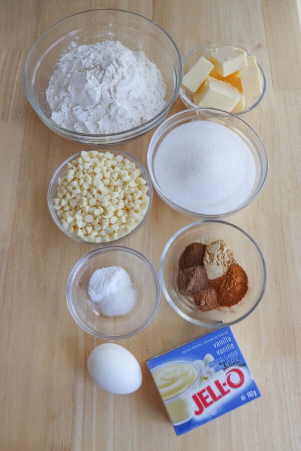 Ingredients for pumpkin spice pudding cookies in clear glass bowls on a wooden table.