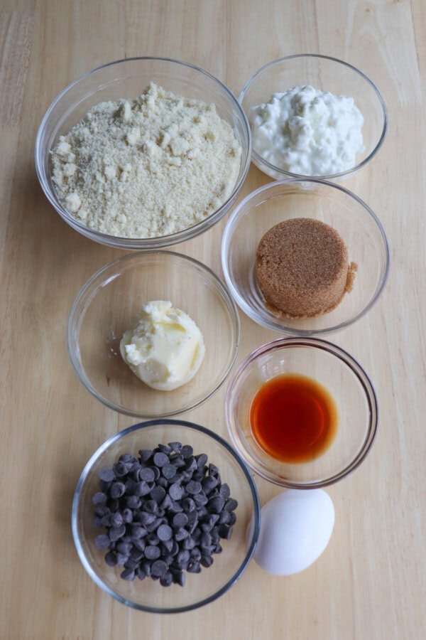 Ingredients for cottage cheese cookies in clear glass bowls on a wood table.