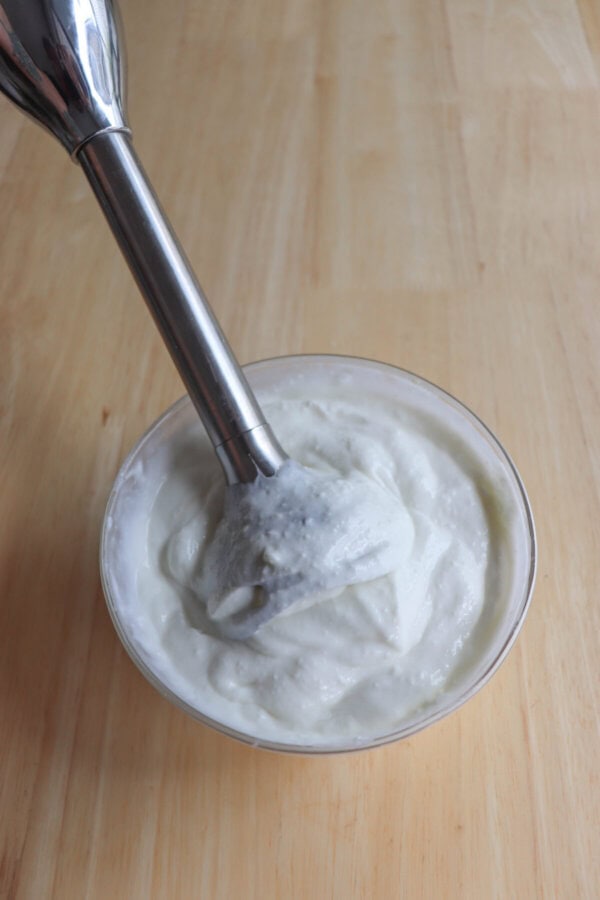 Cottage cheese blended in a clear glass bowl with a hand held blender.