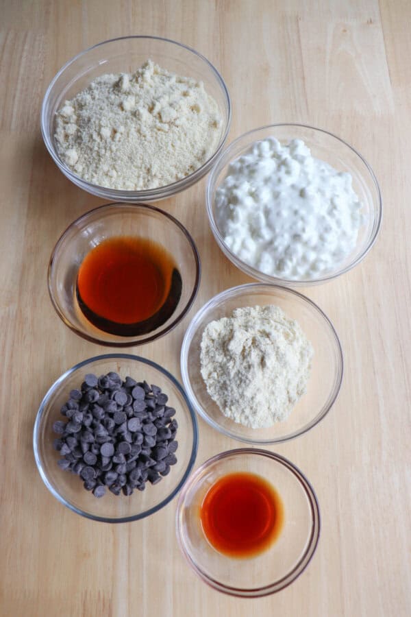Ingredients for cottage cheese protein balls in clear glass bowls on a wooden table.