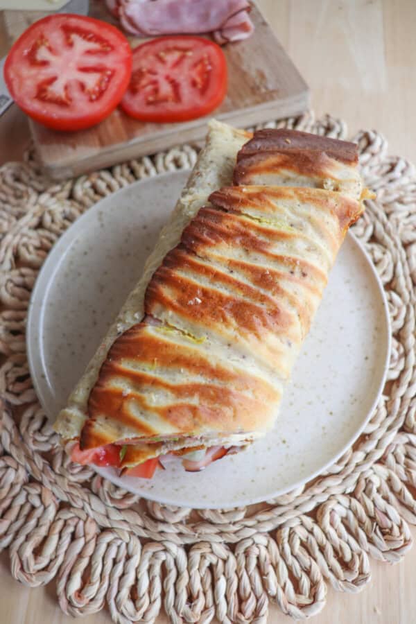 Cottage cheese flatbread wrap filled with ham, tomato and lettuce on a white plate.